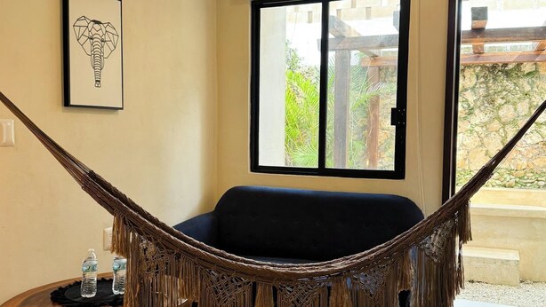 A room with a hammock, a black sofa, a framed picture, and a patterned rug. - Esencia Valladolid Hotel (Valladolid)