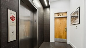 Un ascensor con un letrero que indica uso para bomberos, una puerta con la etiqueta '201' y un cuadro en la pared.