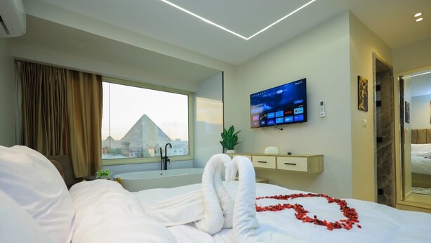 A hotel room with a bed, a TV, a window with a view of a pyramid, and a bathroom with a bathtub. - First site of pyramids view hotel (Giza Governorate)