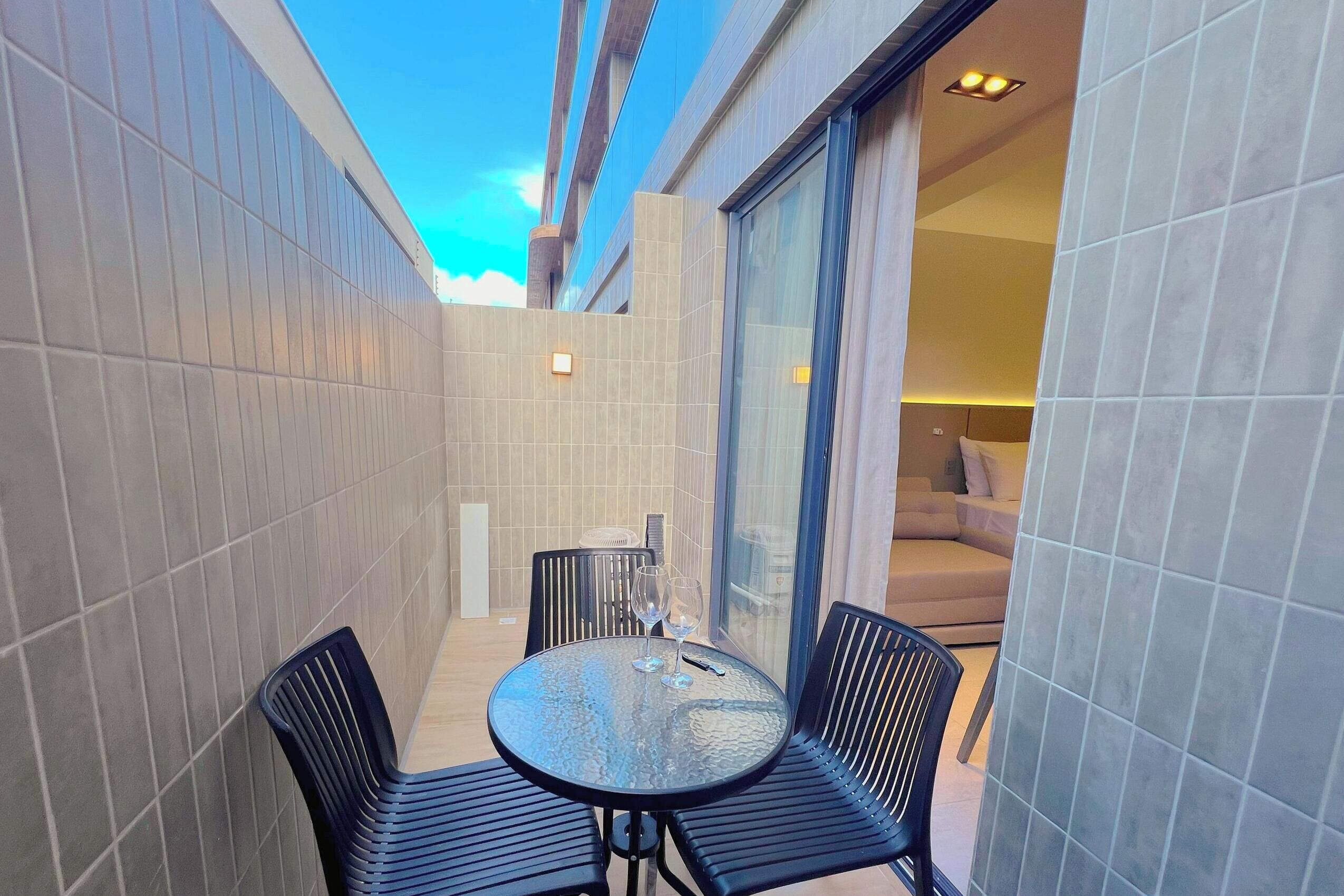 Un pequeño patio al aire libre con una mesa redonda y dos sillas, una puerta de vidrio que da a una habitación y paredes con baldosas.