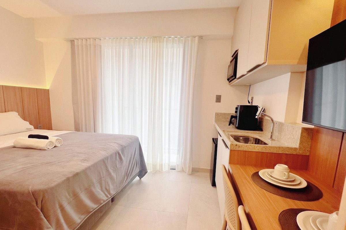 A hotel room with a bed, a desk with a coffee maker, a TV, and a window with curtains.