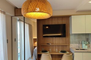 A modern hotel room with a dining area, a TV mounted on the wall, and a kitchen area.