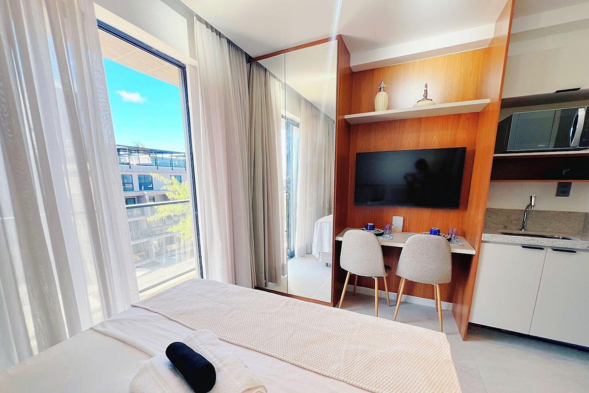 A hotel room with a bed, a desk, a chair, a TV, a microwave, and a view of the outside.