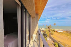 Ein Balkon mit Blick auf den Strand, ein Bett mit weißer Bettdecke und ein weißes Klimagerät.