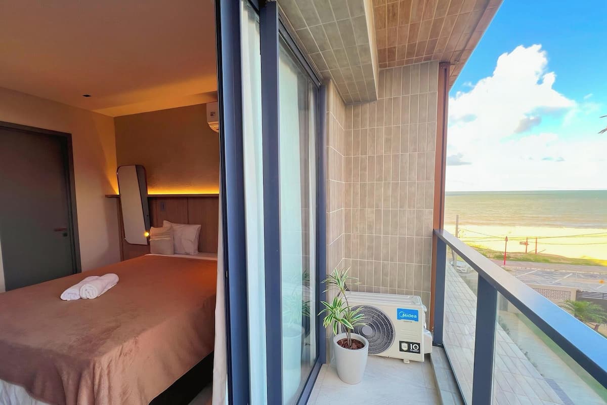 A hotel room with a bed, a potted plant, and a view of the beach.