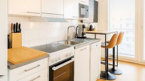 A modern kitchen with white cabinetry, a built-in oven, a stovetop, and a sink. There is a small dining area with two chairs and a table. - Modern and cozy studio just a few minutes from Rovaniemi city center. (Rovaniemi)