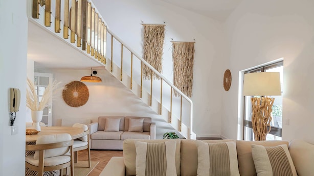 A modern living room with a staircase, a sofa, a dining table, and a hanging light fixture. - Ma-la Beach House by HostWise (Marinhas)