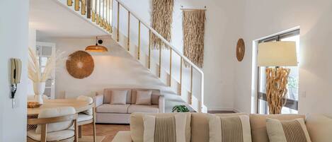 A modern living room with a staircase, a sofa, a dining table, and a hanging light fixture.
