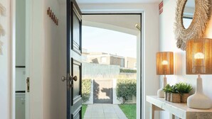 A hallway with a door leading to a garden, a console table with lamps, and a decorative mirror on the wall. - Ma-la Beach House by HostWise (Marinhas)