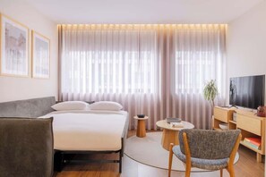 Ein Hotelzimmer mit Bett, Fernseher, Schreibtisch, Stuhl und Vorhängen.