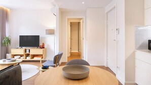Een moderne woonkamer met een flatscreen televisie, een houten tv-meubel, een eettafel met een schaal en een bank.