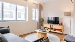 Een moderne woonkamer met een grote televisie, een houten tv-meubel en een grijze bank.