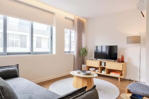 Ein modernes Wohnzimmer mit einer Couch, einem Fernseher, einer Holzkonsole und einer Pflanze.