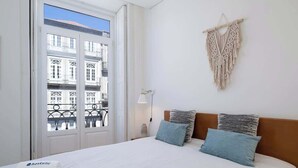 Ein Hotelzimmer mit einem Bett, einer Wanddekoration aus Makramee und Blick auf Gebäude durch ein Fenster.