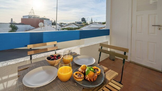 A balcony with breakfast items including toast, a bowl of berries, and orange juice. - Sunlit Balcony & Open Space Flat by HostWise (Albufeira)