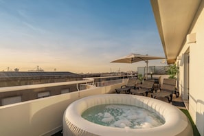 Una terraza en la azotea con jacuzzi, mobiliario exterior y una vista despejada del horizonte de la ciudad.
