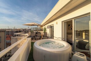 Un balcón moderno con jacuzzi, mobiliario exterior y vista a la ciudad.