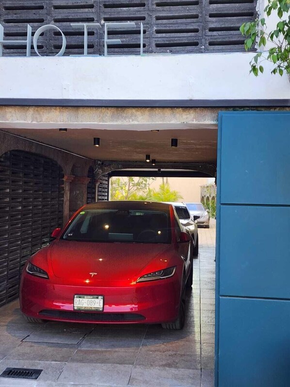 A red Tesla parked in a garage with a blue door and a black wall with a window. - Hotel Miranthia Cuernavaca Adults - Only (Cuernavaca)