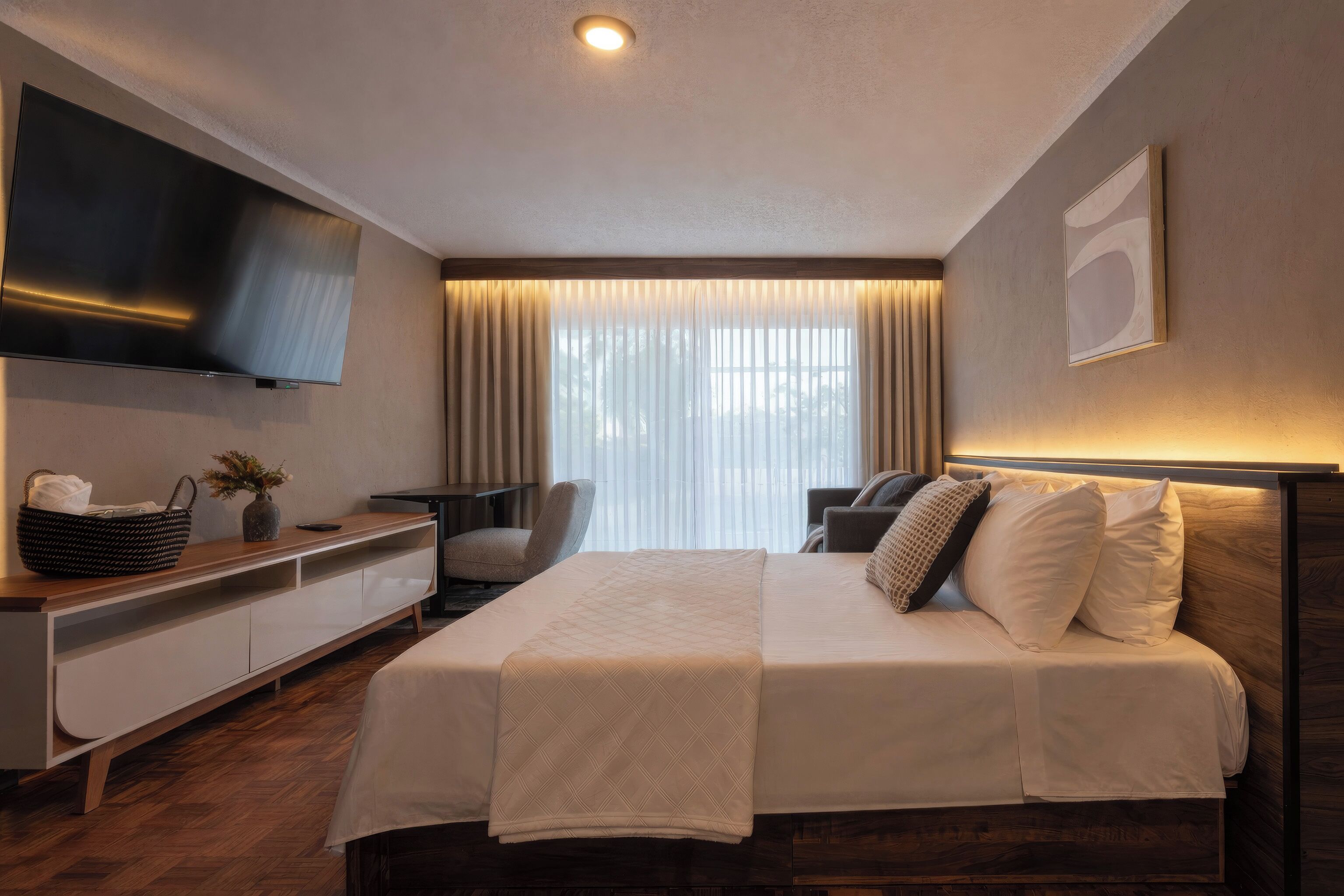 Una habitación de hotel moderna con una cama grande, un televisor de pantalla plana en la pared, un escritorio con una silla y una ventana con cortinas.