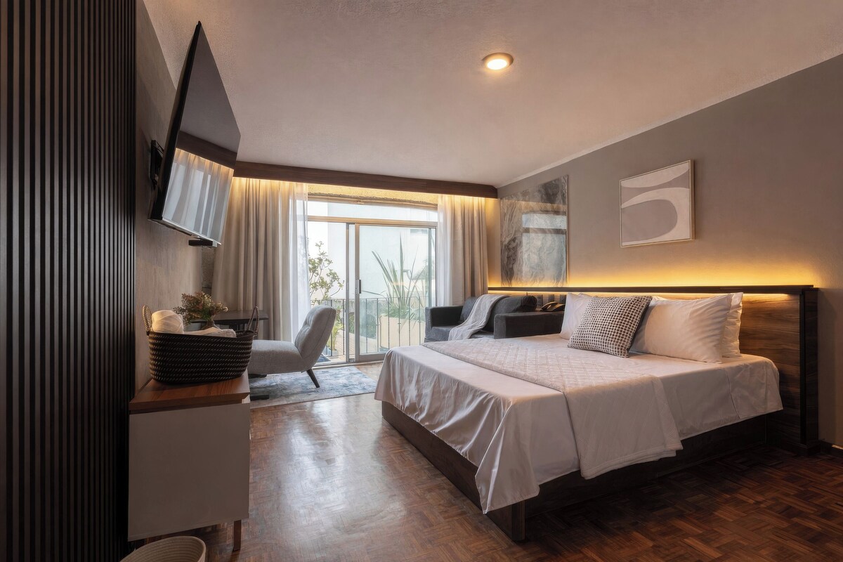 A modern hotel room with a bed, a desk, a chair, and a television.