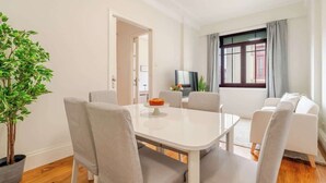 A modern living room with a white table, grey chairs, a potted plant, a sofa, and a TV. - Modern & Cozy Flat with Workspace by HostWise (Porto)