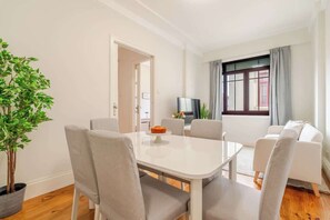 Ein modernes Wohnzimmer mit Esstisch, Stühlen, einer Couch, einem Fernseher und einer Zimmerpflanze.