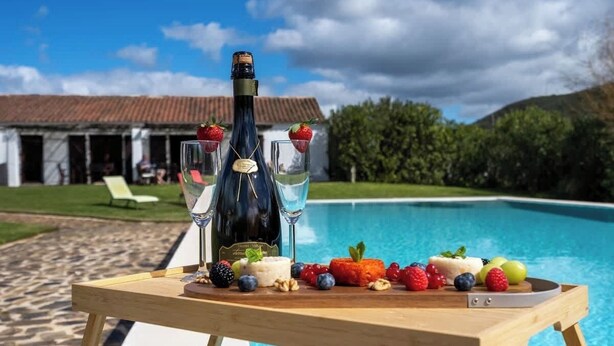 Una mesa de madera con una botella de champán, dos copas y una variedad de frutas y frutos secos.