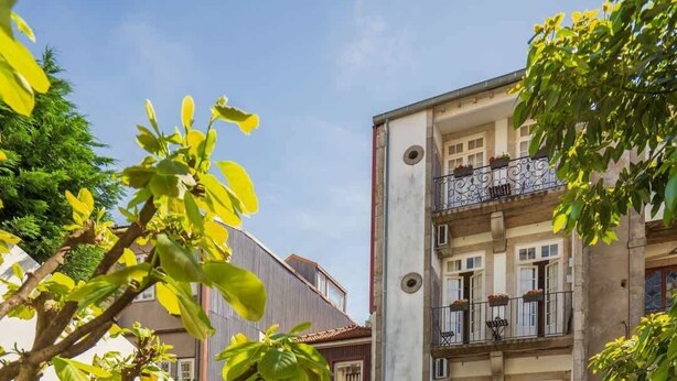 A courtyard with wooden furniture and potted plants, surrounded by a building with balconies and a white wall. - Porto Lounge Hostel - Cozy Bright Room w Balcony (Porto)