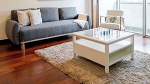 Una sala de estar moderna con un sofá gris, una mesa de centro de vidrio y una alfombra blanca.