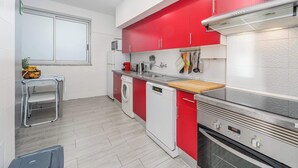 A compact kitchen with red and white cabinetry, a built-in oven, and a washing machine. - Beachfront Flat & Panoramic Sea View by HostWise (Luz)