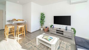 A modern living room with a TV, wooden stools, a coffee table, and a grey sofa. - Beachfront Flat & Panoramic Sea View by HostWise (Luz)