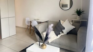 A modern living room with a grey sofa, a round mirror, and a small table with a vase. - Apartment with balcony in Ferndale, Randburg. Stylish, secure and comfortable. (Randburg)