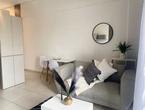 A modern living room with a grey sofa, a round mirror, and a small table with a vase. - Apartment with balcony in Ferndale, Randburg. Stylish, secure and comfortable. (Randburg)