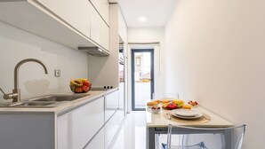 A modern kitchen with white cabinets, a stainless steel sink, and a dining area with a table set for two. - Sleek Apartment with Balcony by HostWise (Porto)