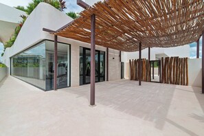 A modern outdoor area with a glass-enclosed structure, a wooden pergola, and a tiled floor. - Modern Tulum Studio - Pool + Rooftop + Gym (Tulum)