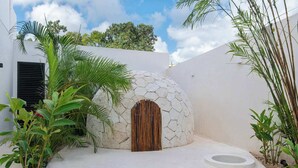 Un edificio moderno caratterizzato da un'originale struttura a cupola in pietra, una porta in legno e vegetazione circostante.
