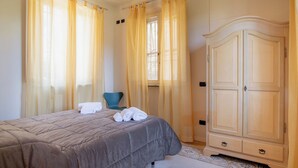 Un dormitorio con cama, una silla, un armario y una ventana con cortinas.