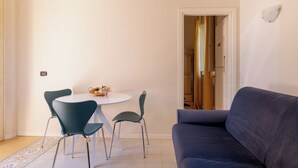 Un comedor con una mesa redonda y cuatro sillas, un sofá, y una puerta que da a otra habitación.