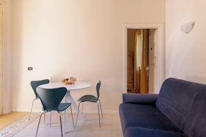 A dining area with a round table and four chairs, a sofa, and a door leading to another room. - Romantic apartment (Lucca)