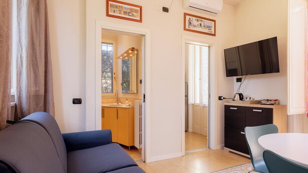 Un espacio habitable compacto con sofá, mesa de comedor, televisor y kitchenette.