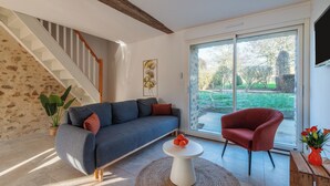 A modern living room with a sofa, a red armchair, a small table, and a staircase.