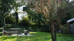 Een tuin met een picknicktafel en bankjes, omringd door bomen en groen.