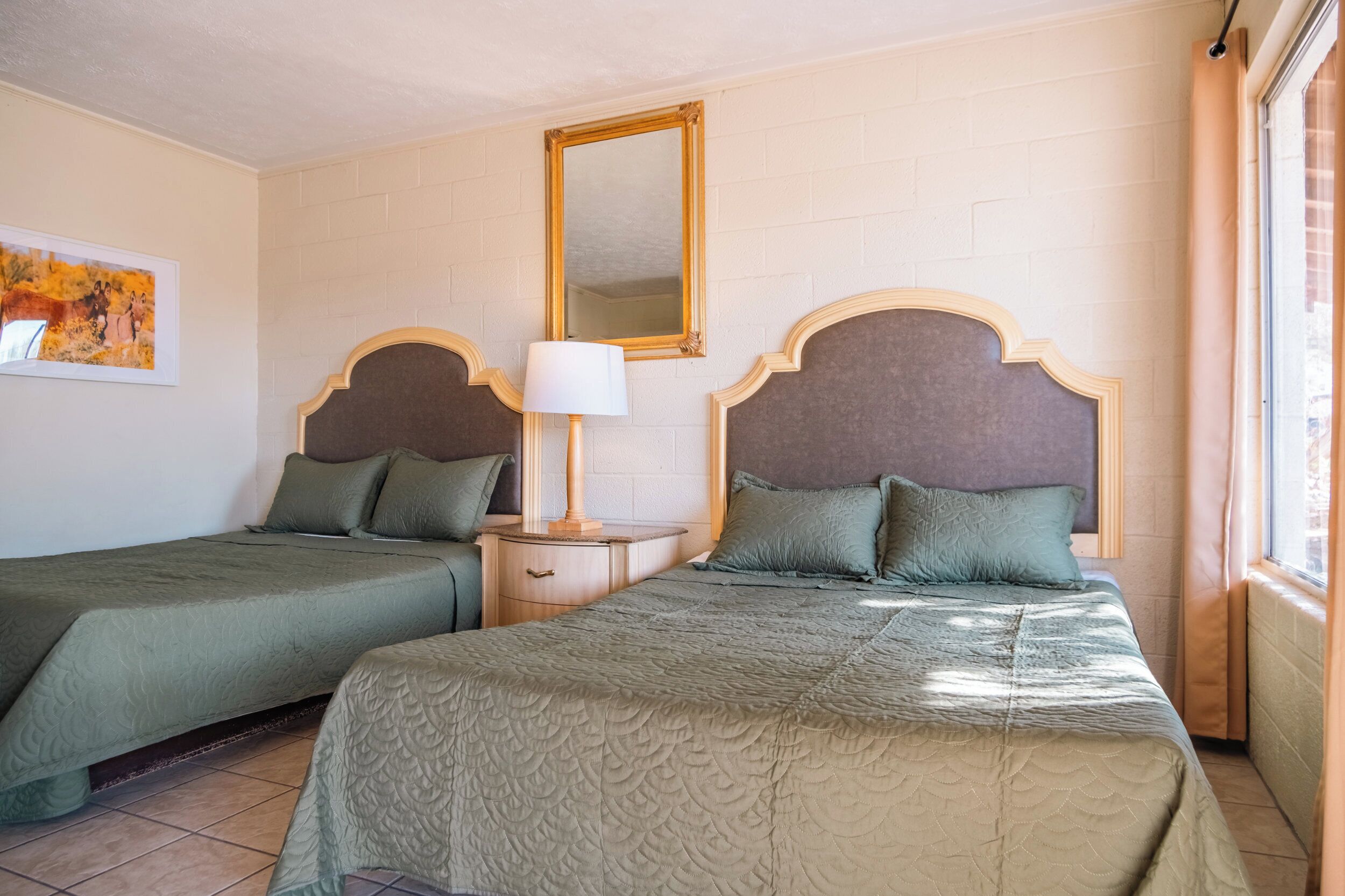 Une chambre d’hôtel avec deux lits, une table de chevet, une lampe, un miroir et un tableau au mur.