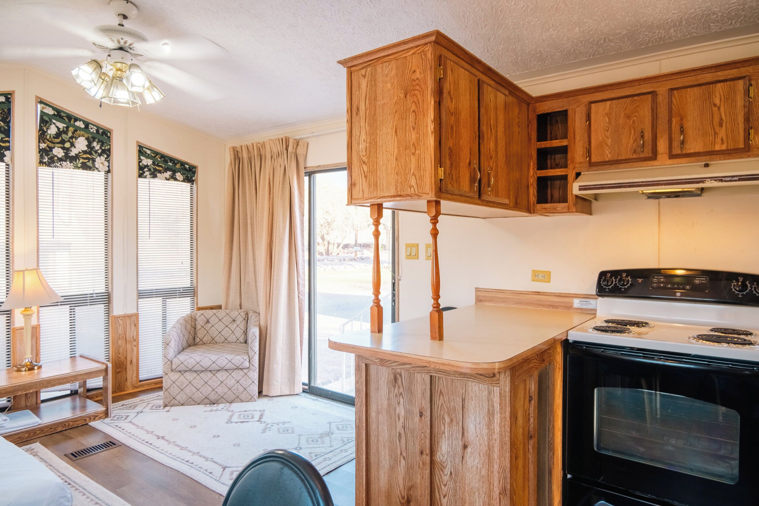 A kitchen with wooden cabinets, a stove, and a dining area with a chair and table.