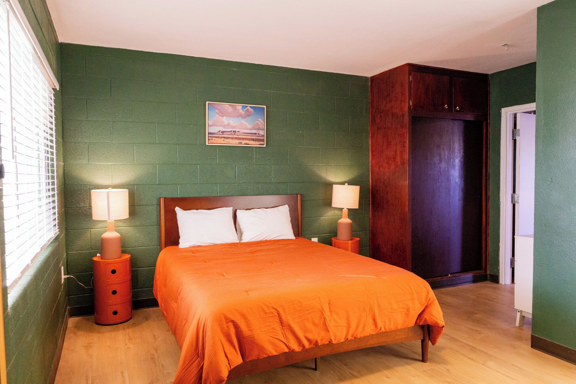 A bedroom with a wooden bed, two bedside tables with lamps, a green brick wall, and a door.