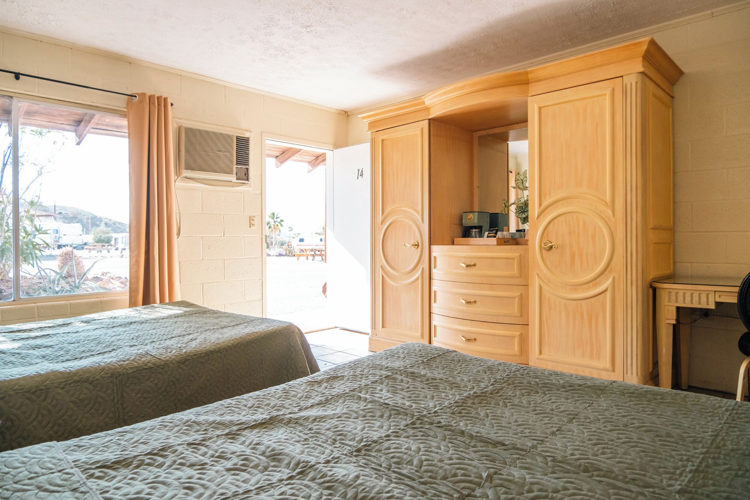 A bedroom with two beds, a wooden wardrobe, a desk, and a window with curtains.