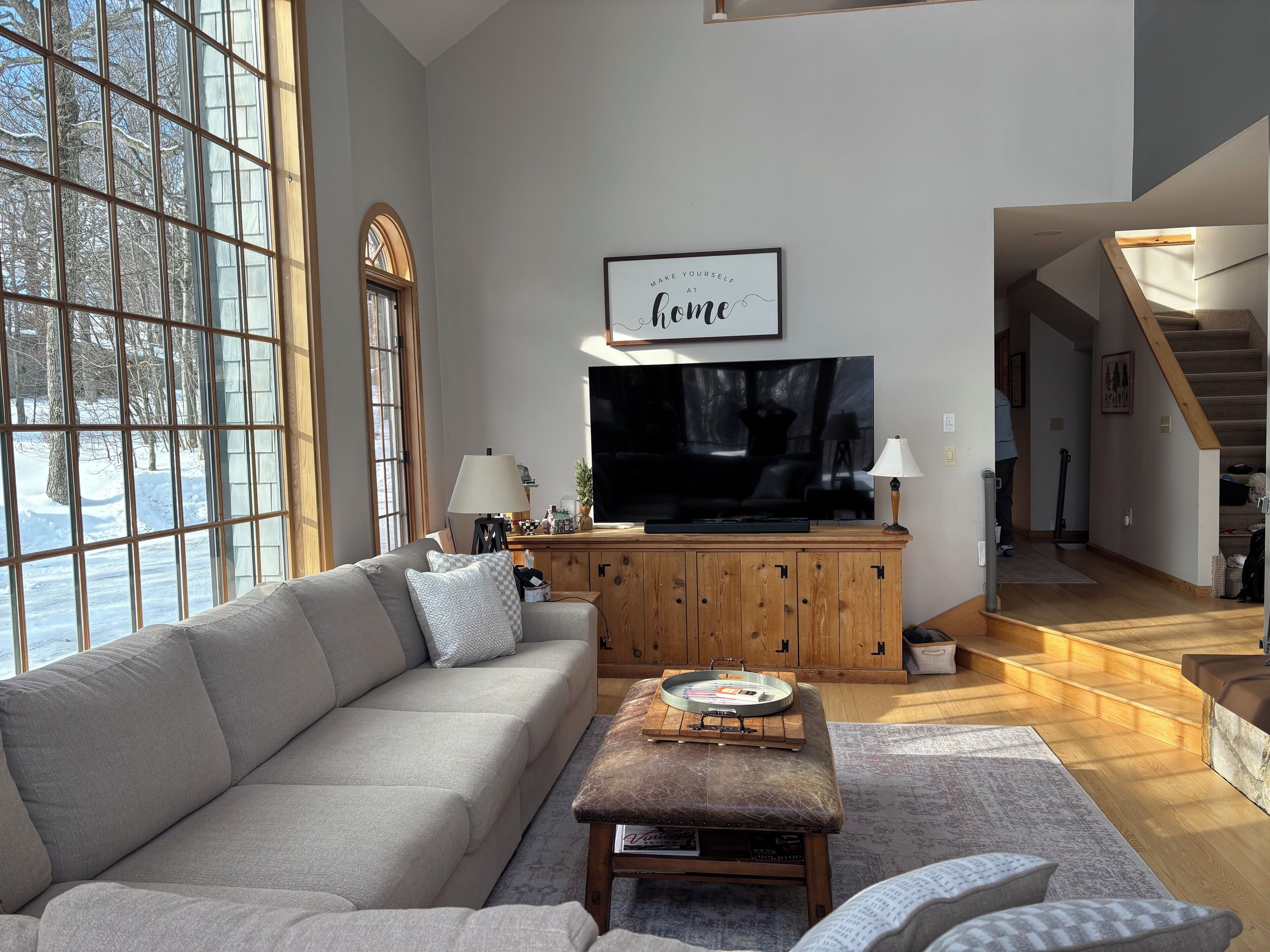 Un salon avec une grande fenêtre, un canapé, une table basse et un téléviseur posé sur un meuble en bois.