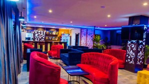 Een moderne lounge met rode en blauwe zitplaatsen, een bar op de achtergrond en decoratieve panelen.