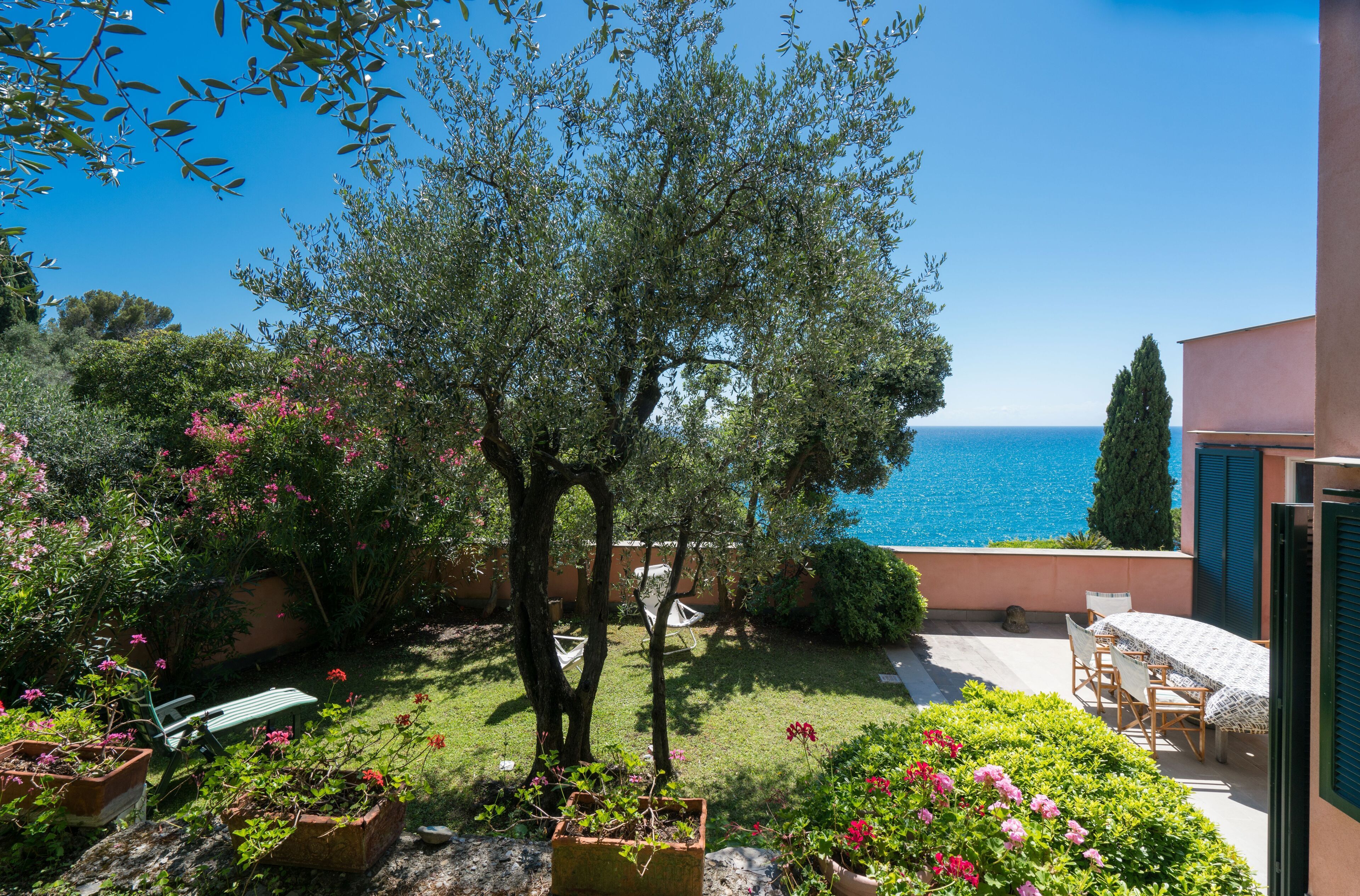 Ein Garten mit Tisch und Stühlen, einem Baum und Blick auf das Meer.