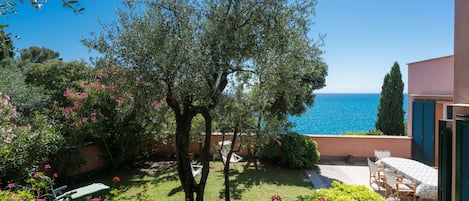 Ein Garten mit Tisch und Stühlen, einem Baum und Blick auf das Meer.